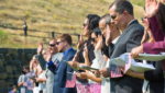 New American citizens holding small U.S. flags raise their right hands to take the Oath of Allegiance at an outdoor naturalization ceremony