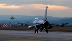Two U.S. Air Force F-16 fighter jets at dusk at Aviano Air Base, Italy, one taxiing on the runway and one coming in to land